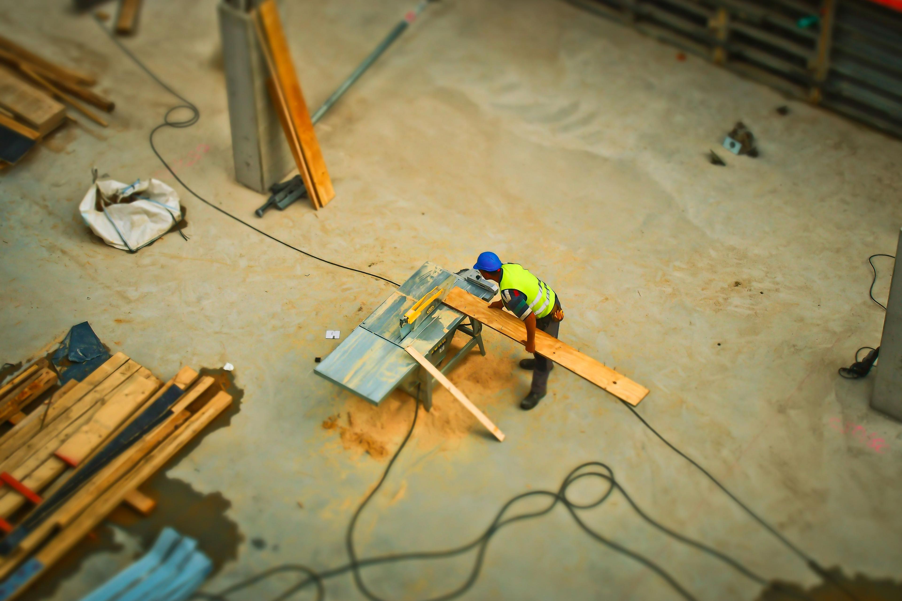Construction worker in high-vis jacket cutting wood with a saw on a concrete construction site.