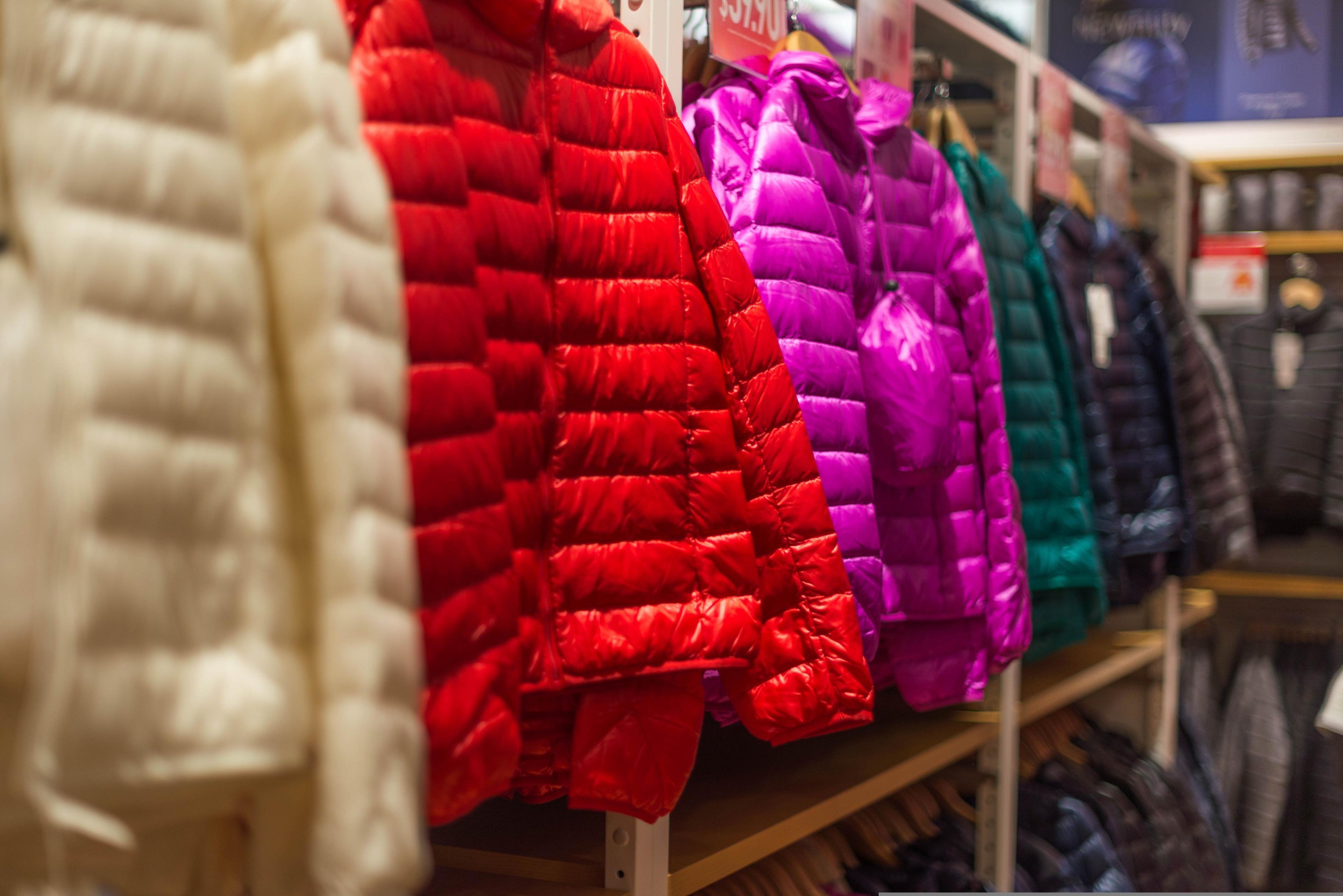 Colorful puffer jackets in white, red, and purple hanging on a retail rack.