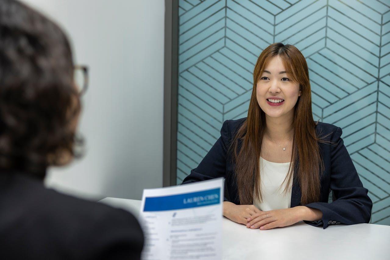 Smiling woman in a blazer sits at a desk during a professional interview.